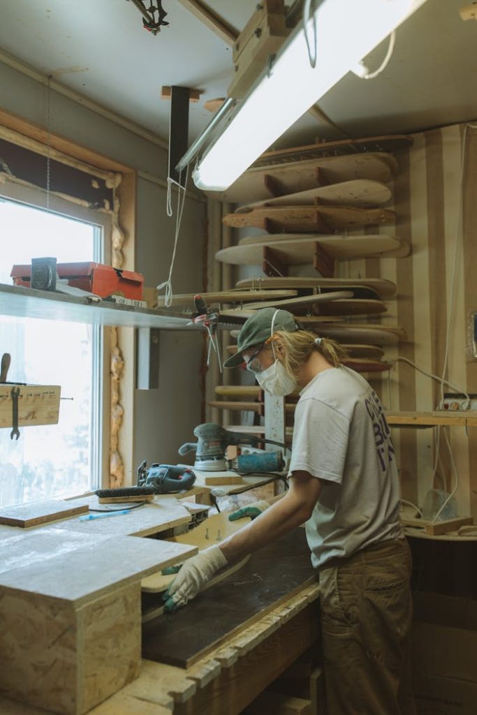 An artisan shaping a skateboard in a workshop, highlighting woodworking craftsmanship.